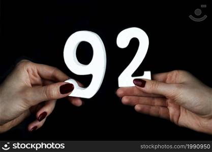 On a black background, female hand with numbers ninety-two.. To female hands the figure of ninety-two.