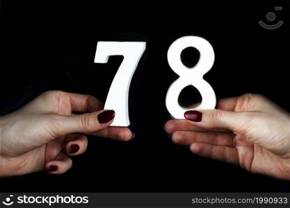 On a black background, female hand with numbers seventy-eight.. To female hands the figure of seventy-eight.