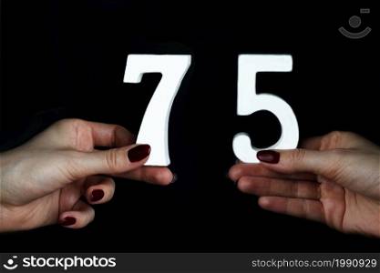 On a black background, female hand with numbers seventy-five.. To female hands the figure of seventy-five.