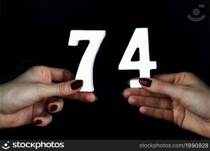 On a black background, female hand with numbers seventy-four.. To female hands the figure of seventy-four.