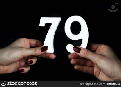 On a black background, female hand with numbers seventy-nine.. To female hands the figure of seventy-nine.