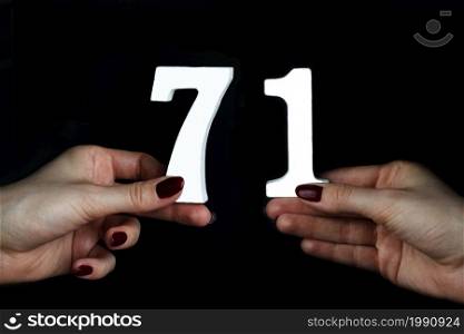 On a black background, female hand with numbers seventy-one.. To female hands the figure of seventy-one.
