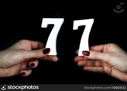 On a black background, female hand with numbers seventy-seven.. To female hands the figure of seventy-seven.