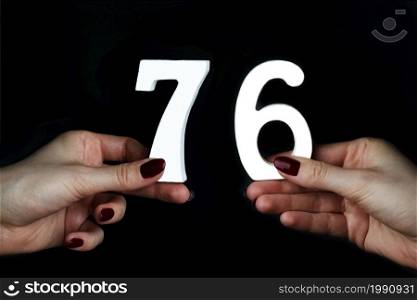 On a black background, female hand with numbers seventy-six.. To female hands the figure of seventy-six.