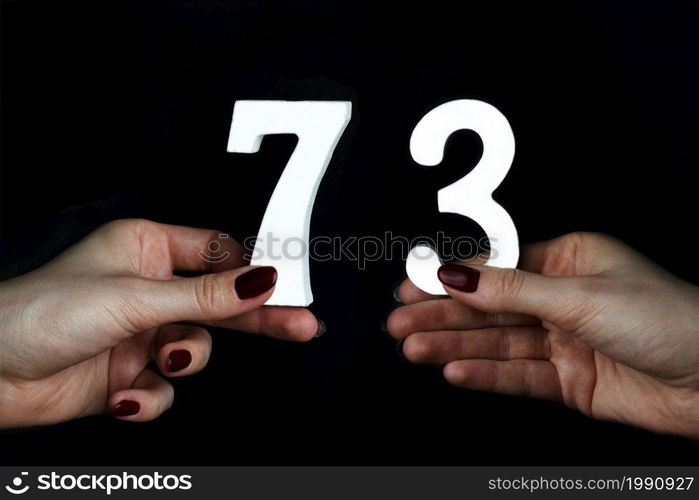 On a black background, female hand with numbers seventy-three.. To female hands the figure of seventy-three.