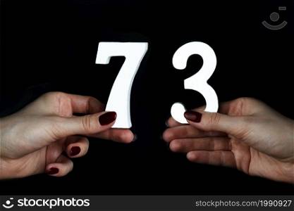 On a black background, female hand with numbers seventy-three.. To female hands the figure of seventy-three.