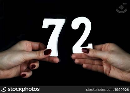 On a black background, female hand with numbers seventy-two.. On the female palms figure seventy-two.