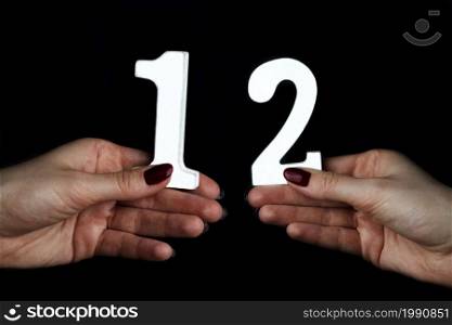 On a black background, female hand with numeral twelve.. To female hands the number twelve.