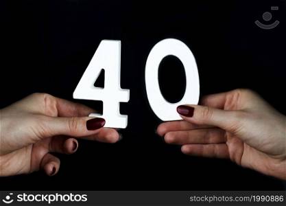 On a black background, female hand with the number forty.. To female hands the number forty.