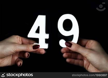 On a black background, female hand with the number forty-nine.. To female hands the number forty-nine.
