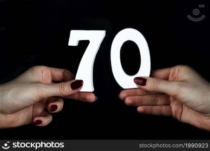 On a black background, female hand with the number seventy.. To female hands the number seventy.