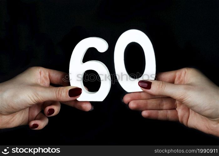 On a black background, female hand with the number sixty.. On the female palms figure sixty.