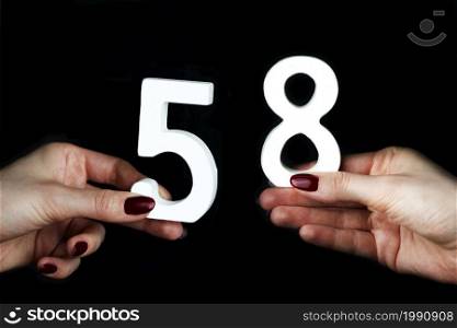 On a black background, female hand with the number sixty-five.. On the female palms figure sixty-five.