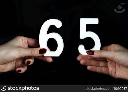 On a black background, female hand with the number sixty-five.. On the female palms figure sixty-five.