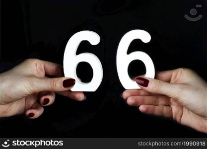 On a black background, female hand with the number sixty-six.. To female hands the number sixty-six.