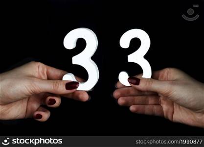 On a black background, female hand with the number thirty-three.. On the female palms figure thirty-three.