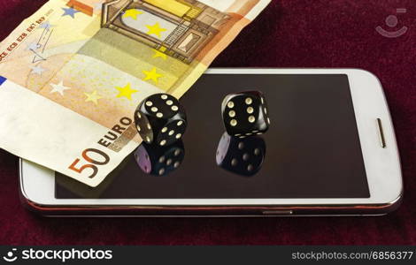 On a crimson cloth is a smartphone. On the mirror screen smartphone is part of the banknote and dice for the game of poker. Cubes reflected in the screen of your smartphone.