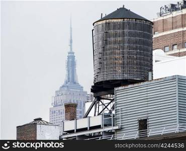 On a hazy day in New York, The Empire State Building rises in over a classic wooden water tower on the roof of a building.