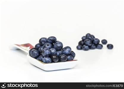 On a light background lie in a porcelain spoon lie large berries of blueberries