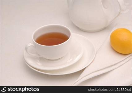 on a napkin cup of tea with lemon in a saucer and teapot. tea saucer cup and napkin