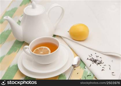 on a napkin cup of tea with lemon in a saucer and teapot. tea saucer cup and napkin