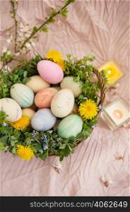On a pastel bedspread is a basket of grass and bright flowers. The basket contains Easter eggs painted with watercolors in beautiful pastel colors. On a pastel bedspread is a basket of grass and bright flowers. The basket contains Easter eggs painted with watercolors in beautiful pastel colors.