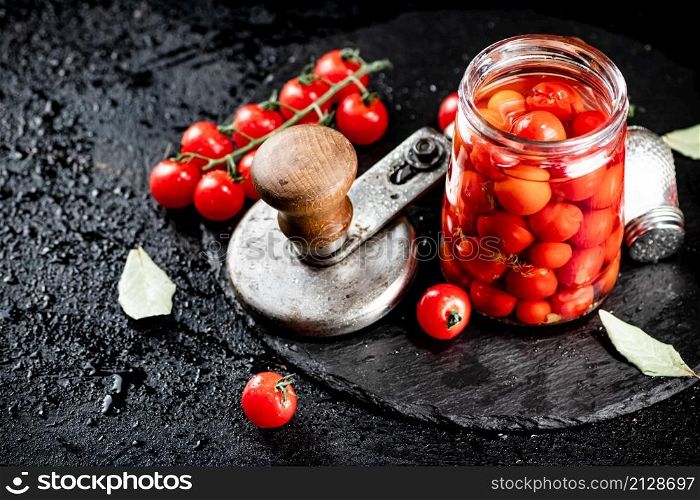 On a stone board are pickled tomatoes in a jar. On a black background. High quality photo. On a stone board are pickled tomatoes in a jar.