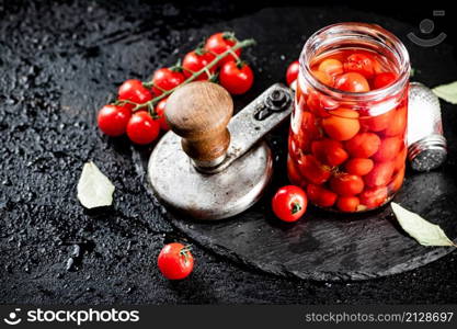 On a stone board are pickled tomatoes in a jar. On a black background. High quality photo. On a stone board are pickled tomatoes in a jar.