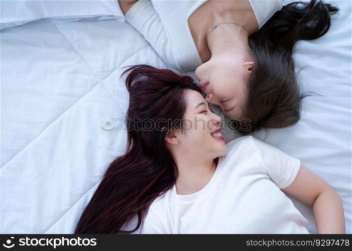 On a white bed, an LGBT couple is gently kissing each other&rsquo;s foreheads.