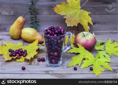 On a wooden surface lie autumn leaves in a glass sprinkled on cranberry and apple and pear lie