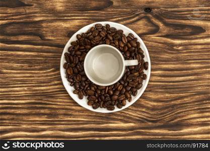 On a wooden surface there is a white saucer with coffee beans and an empty coffee cup