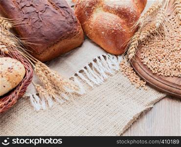 On a wooden table covered with burlap and linen napkins. On a napkin placed rye and wheat bread. Wooden cutting board and basket of bread on a sacking. Ears and grain on a wooden cutting board. Baking lying in a wicker basket.. Rye spikelets, wheat bread, bun in the basket. Canvas, burlap, wooden table, wooden cutting board.