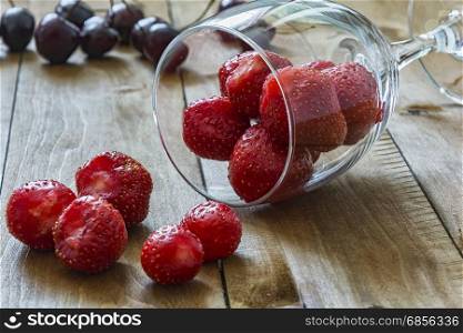 On a wooden table lies a glass wine glass with berries of strawberries and red apple