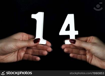 On black background female hands with number fourteen.. On the female palms figure fourteen.