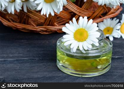 On dark boards near the basket with chamomile flowers there is a bank of light chamomile essential oil.. On the boards near the basket with chamomile flowers there is a bank of light chamomile essential oil.