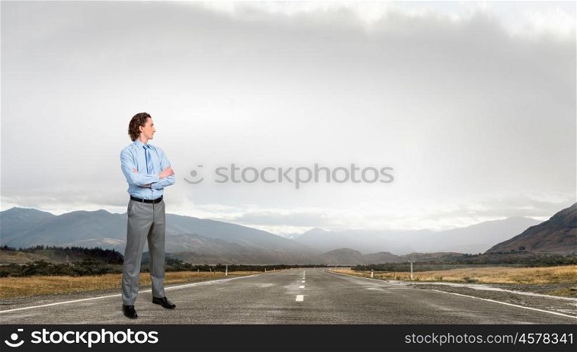 On his way to success. Young confident businessman with arms on chest on asphalt road