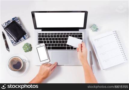 On-line shopping concept mock up - desktop with laptop and hands holging credit card, copy space on empty screen of phone, notebook and plastic card. On-line shopping concept
