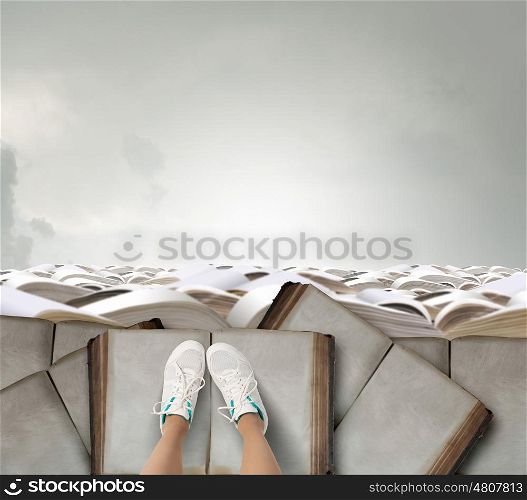 On pile of books. Top view of female legs in sport shoes standing on pile of books