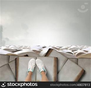 On pile of books. Top view of female legs in sport shoes standing on pile of books
