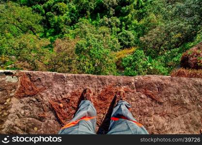 On the edge concept with man standing on cliff ledge looking down at forest