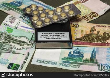 On the gray surface is currency notes of different denomination, a pack of cigarettes and drugs lie on it