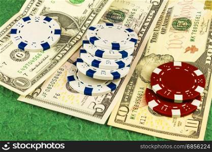 On the green cloth of the poker table is one, five and ten dollar bills and white and red chips