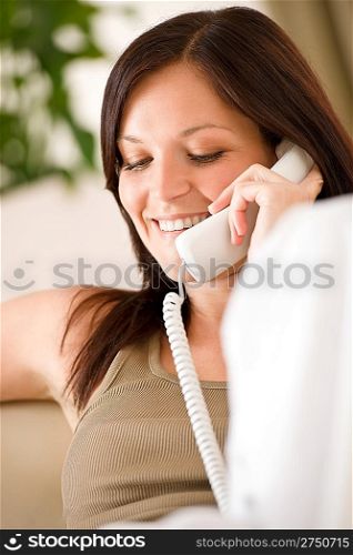 On the phone home - Smiling woman on sofa calling, plant in background