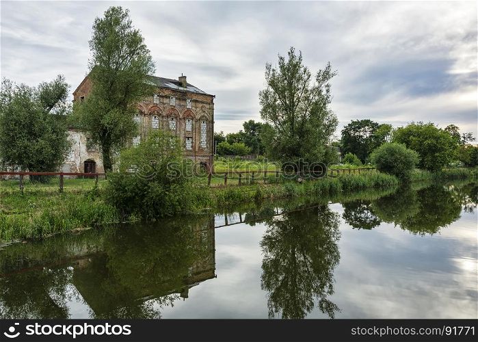 On the river bank is an abandoned old brick building and is reflected in the surface of the water