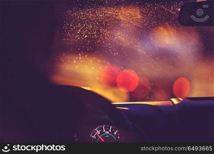On the road on a rainy night, rain drops on the windshield limit the visibility of the road, blurred lights of urban traffic jams, rainy nighttime on the city streets. On the road on a rainy night