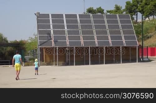 On the street of city Perea, Greece father photographed on a mobile phone his son near solar panels