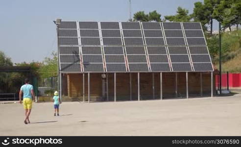 On the street of city Perea, Greece father photographed on a mobile phone his son near solar panels