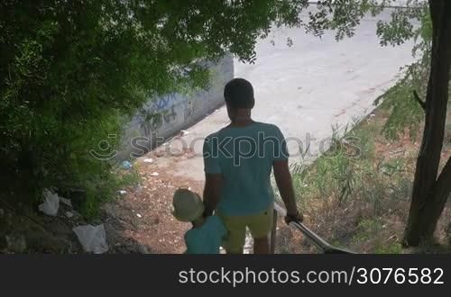 On the street of city Perea, Greece in park down the stairs father holding for hand of his son and going away