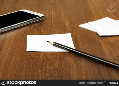 On the surface of the table is a smartphone and sheets for notes with a pencil