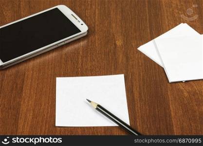 On the surface of the table lie a sheet for notes, a pencil and a smartphone
